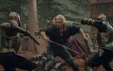Geralt wields a sword and axe as soldiers attack him on each side in a fight scene from The Witcher season 3